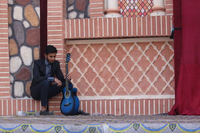 Full length of man sitting against wall