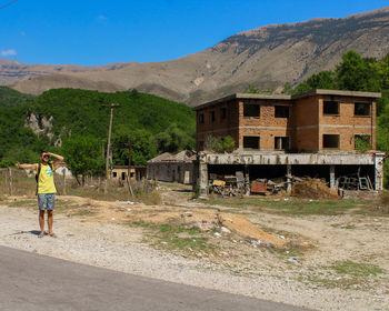 Rear view of man standing by building against sky