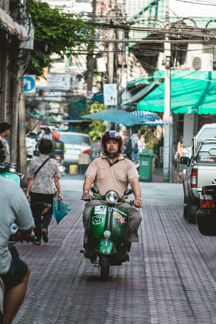 city, street, architecture, real people, mode of transportation, transportation, men, incidental people, building exterior, people, lifestyles, built structure, city life, land vehicle, travel, day, full length, road, scooter, outdoors