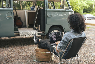 Young man using laptop while sitting on chair in front of van