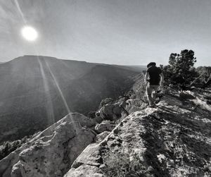 Rear view of man standing on rock against sky