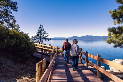 Couple walking on footbridge over lake against clear sky