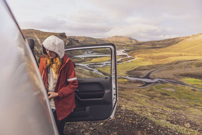 Young woman getting off a car in front of valley in highlands iceland