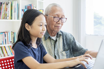 Granddaughter and grandfather using laptop at home