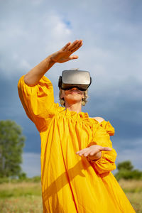 Young woman with yellow umbrella standing on land against sky