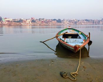 Boat moored on sea by city against sky