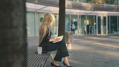 Businesswoman holding digital tablet sitting on bench outdoors