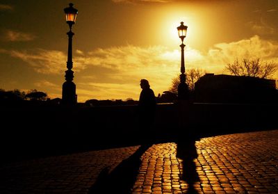 Silhouette man walking on street against sky during sunset