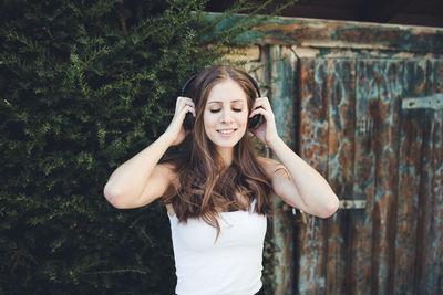 Young woman with closed eyes listening to music via headphones outdoors. spring or summer time