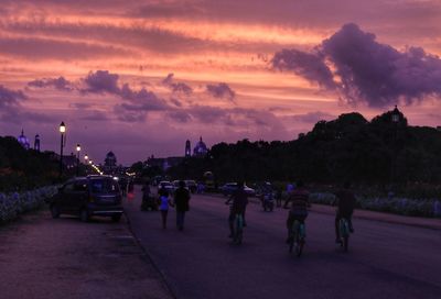 People on street in city against sky at sunset