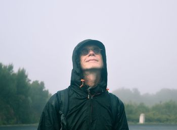 Mature man wearing hoodie looking up standing against sky