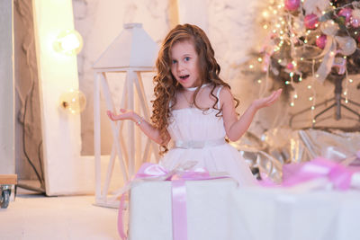 A beatiful girl with curly hair in white dress is surprising of christmas box gift