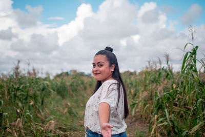 Portrait of smiling young woman standing on field against sky