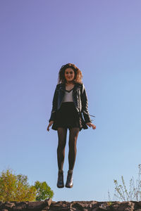 Full length portrait of young woman against clear blue sky