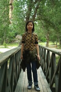 Full length portrait of young woman standing on footbridge at park