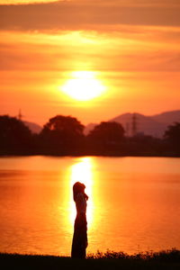 Silhouette of man standing against orange sunset sky