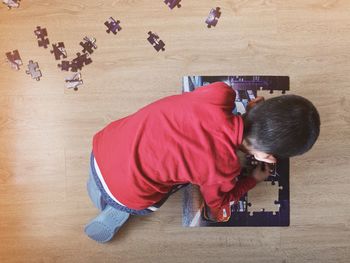 High angle view of boy solving puzzle on hardwood floor