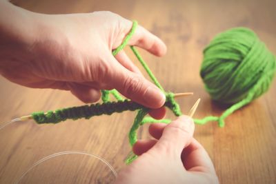 Cropped hands knitting green wool on table at home