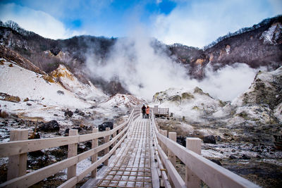 Footbridge on snowcapped mountains against sky