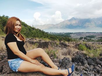 Beautiful young woman sitting on land against sky