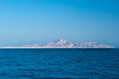 Scenic view of sea and mountains against clear blue sky