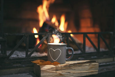 A mug of hot tea, coffee, cocoa, stands on the fireplace in which the fire is burning