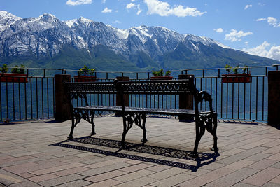 Chairs on bench by snowcapped mountains against sky