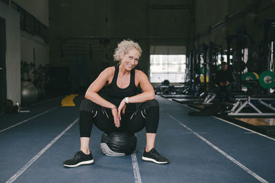 Portrait of smiling woman sitting on medicine ball at gym