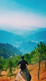 Rear view of man sitting on mountain against sky