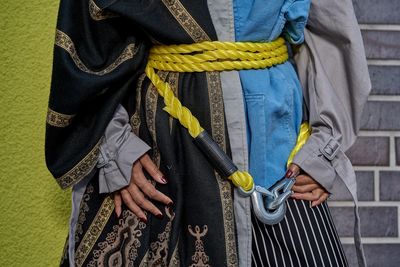 Midsection of man wearing rope standing against wall