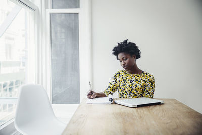 Businesswoman writing in book at desk in board room