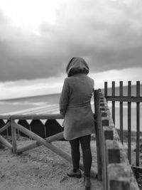 Rear view of woman standing by railing against sea