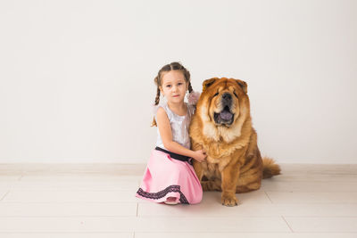 Portrait of girl with dog sitting on wooden floor