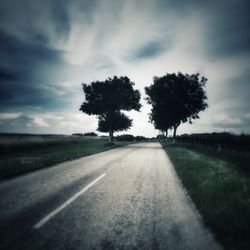 Empty road by field against cloudy sky