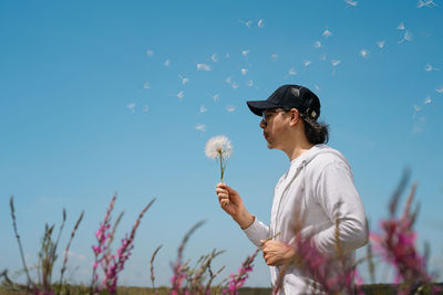 Man blowing dandelion against purple flowers and clear sky