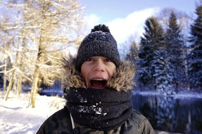 Portrait of teenage boy wearing warm clothing while screaming against lake during winter