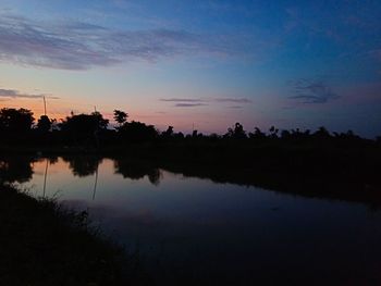 Silhouette trees by lake against sky during sunset