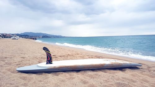 Surfboard on sandy beach against cloudy sky