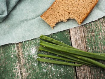 Directly above shot of bread by scallion leaves on wooden table