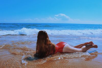 Sensuous woman lying on sea shore at beach against blue sky