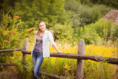 Attractive young woman standing near old wooden fence.