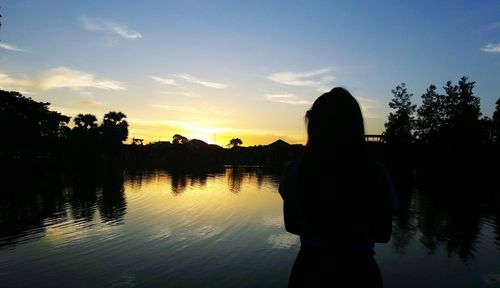 Silhouette woman standing by lake against sky during sunset