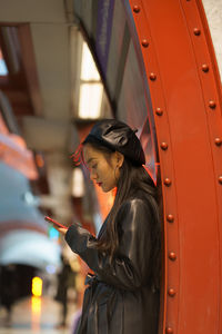 Stylish korean girl checking map, online schedule in smartphone app wait for train at subway station
