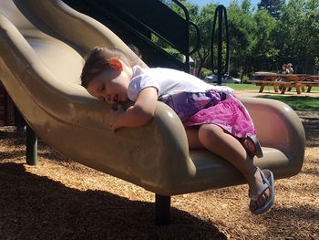 Girl lying on slide in park during sunny day