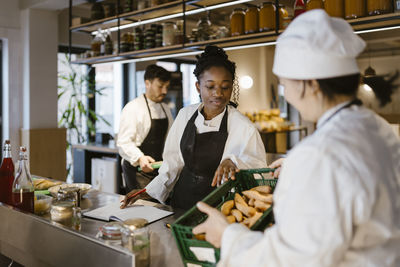 Young chef taking inventory with female colleague at commercial kitchen in restaurant