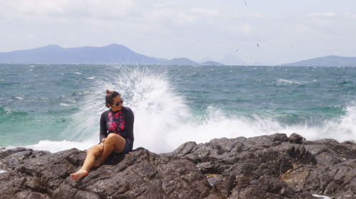 Full length of young woman on rock at beach against sky