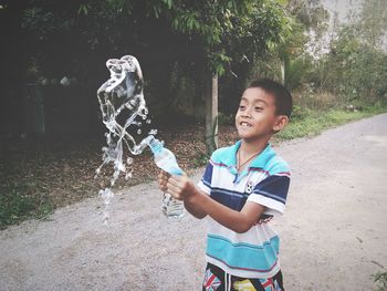 Portrait of boy holding camera while standing against tree