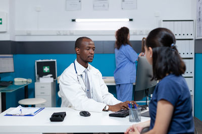 Doctor using computer in clinic while sitting with patient