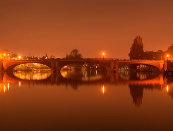 Arch bridge over river in illuminated city at night