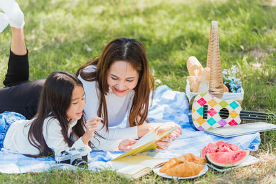Mother and daughter reading book while relaxing on grass at park